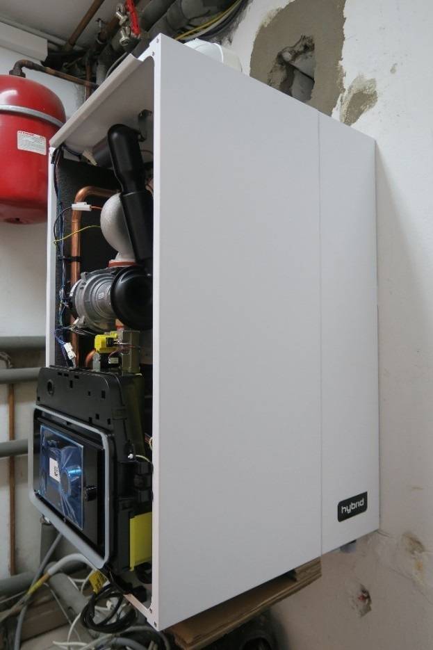 Weißer Hybridkessel mit sichtbaren Bauteilen, wandmontiert im Technikraum - Beispiel für moderne Heiztechnik in der Gebäudetechnik.