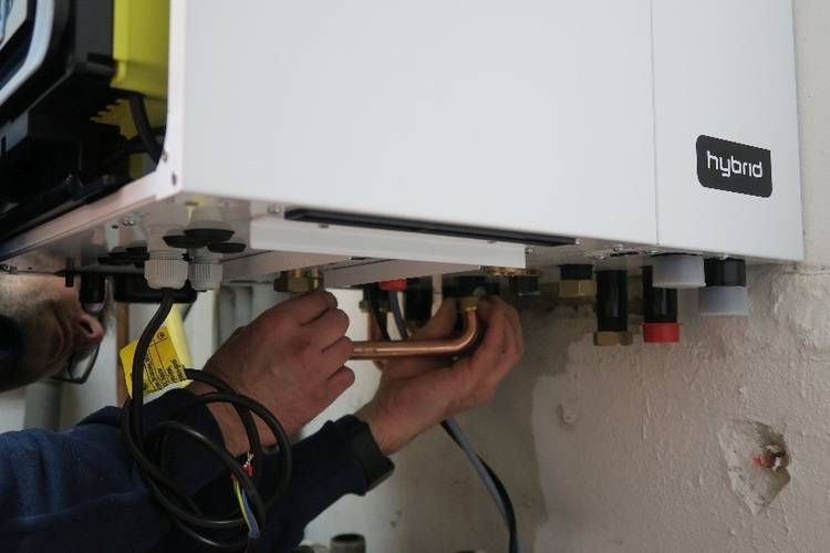 Fachhandwerker installiert oder wartet ein wandhängendes Hybrid-Heizsystem, schließt Rohrleitungen und elektrische Anschlüsse fachgerecht an.