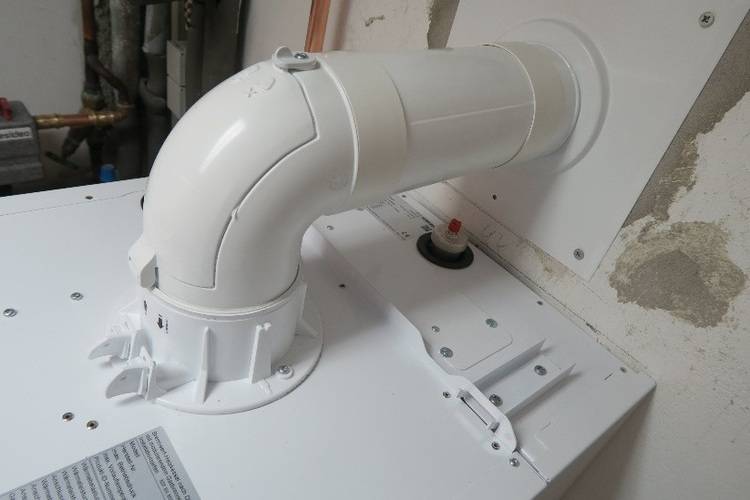 Flexibler, weißer Abluftschlauch fachgerecht am Trockner montiert; Wandanschluss mit sichtbaren Ausbesserungen im Bereich Gebäudetechnik.