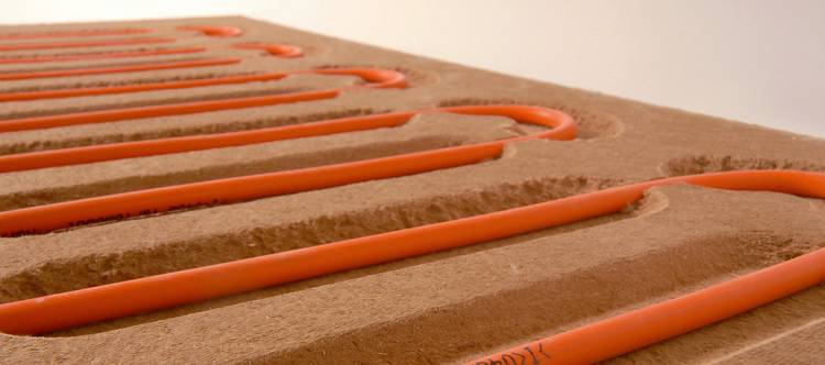 Detailansicht: orangefarbene Heizrohre in gefrästen Dämmplatten für Fußbodenheizung, typische Installation im modernen SHK-Gebäudetechnikbereich.