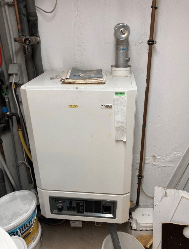 Gas-Brennwertkessel im Technikraum, angeschlossene Rohrleitungen und Abgasführung, Ablage von Dokumenten auf dem Gehäuse.