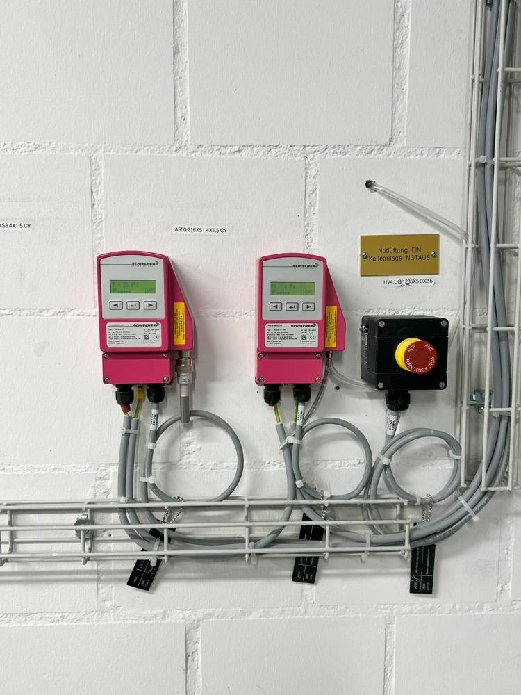 Zwei digitale Steuerungen und ein Not-Aus-Schalter an weißer Wand, mit angeschlossenen Kabeln - Beispiel für Gebäudetechnik-Bedienfelder.