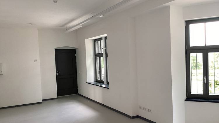 Lichtdurchfluteter, leerer Raum mit weißen Wänden, großen Fenstern und schwarzer Tür - Beispiel für energieeffiziente Gebäudehülle.