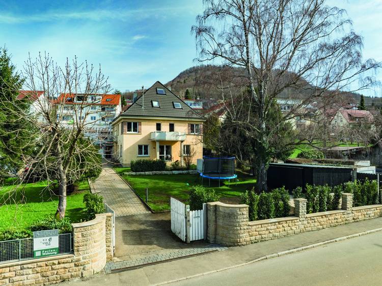 Zweistöckiges Wohnhaus mit Garten, Steinzaun und Bäumen, beispielhaft für moderne Gebäudehülle und energieeffiziente Gebäudetechnik im Wohnbau.