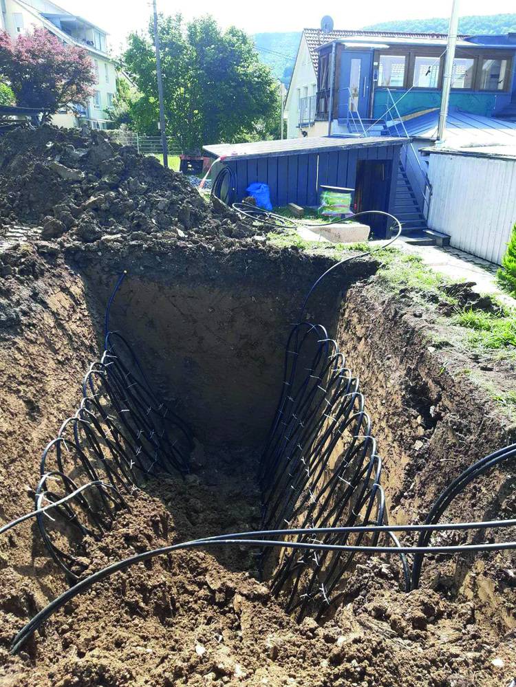 Tiefbaugraben mit verlegten schwarzen Kunststoffrohren für Nah- oder Fernwärmeversorgung, auf Baustelle nahe eines Wohngebäudes.
