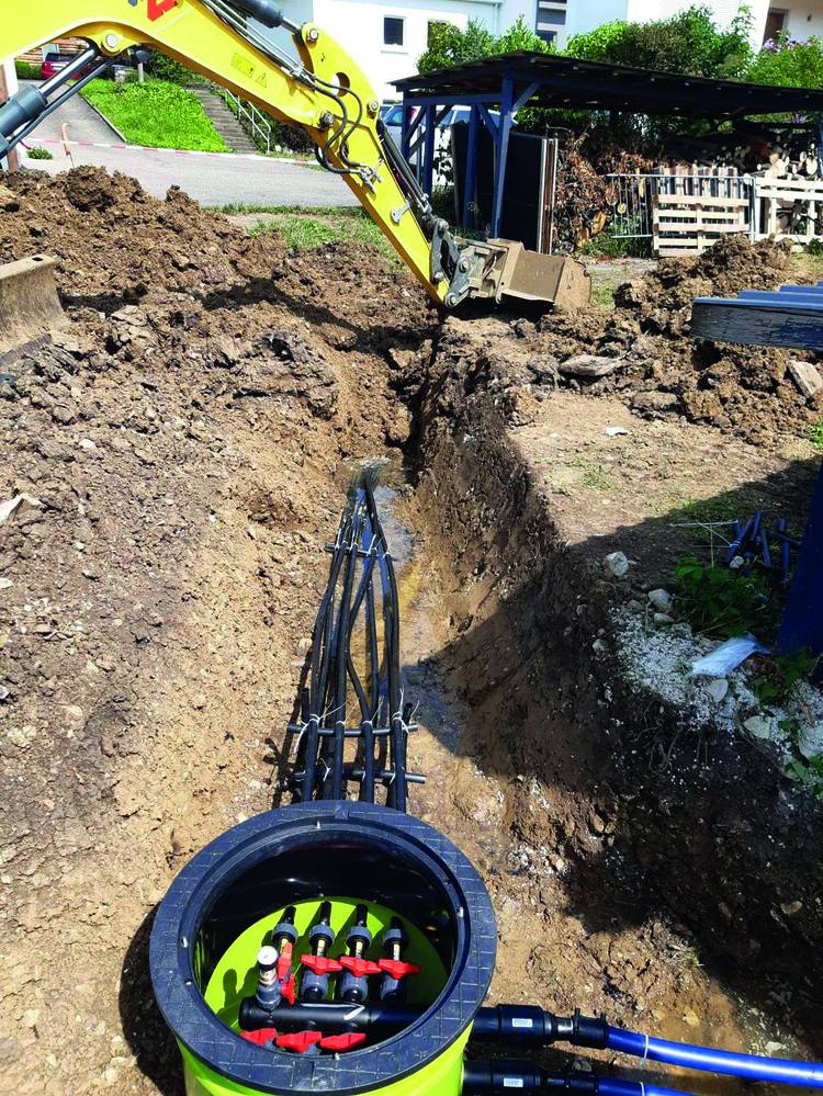 Bagger hebt Graben für Installation von Kabeln und Armaturen in einer unterirdischen Versorgungsbox im Kontext moderner Gebäudetechnik.