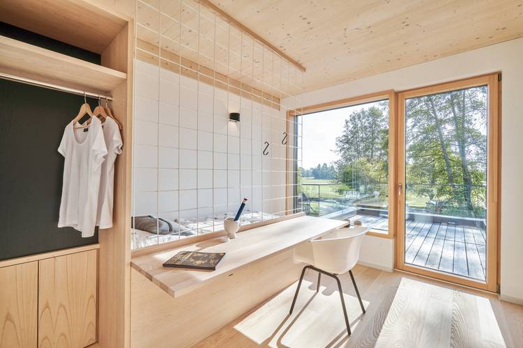Modernes Schlafzimmer mit großem Fenster, Holzschreibtisch und -stuhl, optimaler Tageslichteinfall für energieeffiziente Gebäudetechnik-Lösungen.