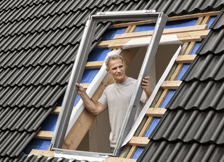 Fachhandwerker montiert ein Dachfenster in das geneigte Ziegeldach eines Gebäudes im Rohbau, Fokus auf Installation und Gebäudehülle.