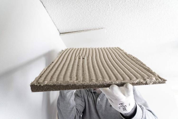 Fachkraft mit weißen Handschuhen positioniert eine gerillte Zementtafel zur Deckenmontage - Trockenbau im Kontext moderner Gebäudetechnik.