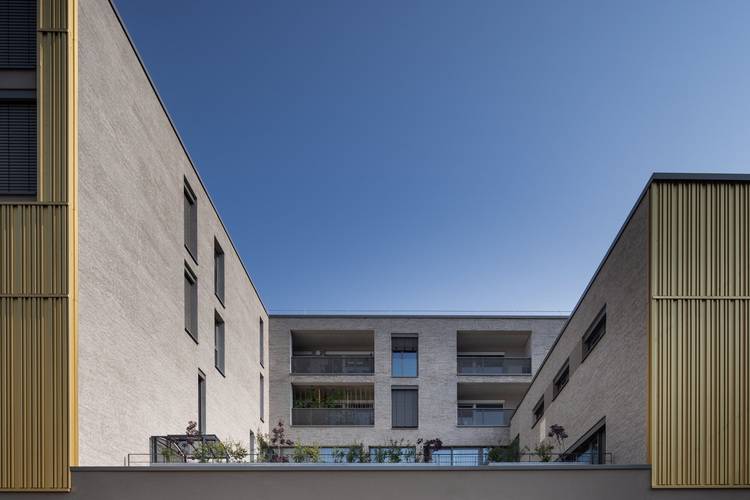Modernes Mehrfamilienhaus mit energieeffizienter Fassade und goldfarbenen Akzenten, Fokus auf Gebäudetechnik, aufgenommen im Innenhof.