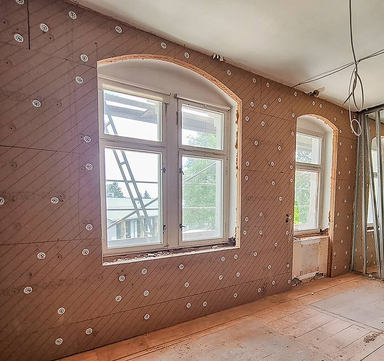 Sanierungsraum mit zwei Rundbogenfenstern, freiliegenden Wänden und sichtbaren Dämmstoffhaltern - Fokus auf energetische Gebäudesanierung.