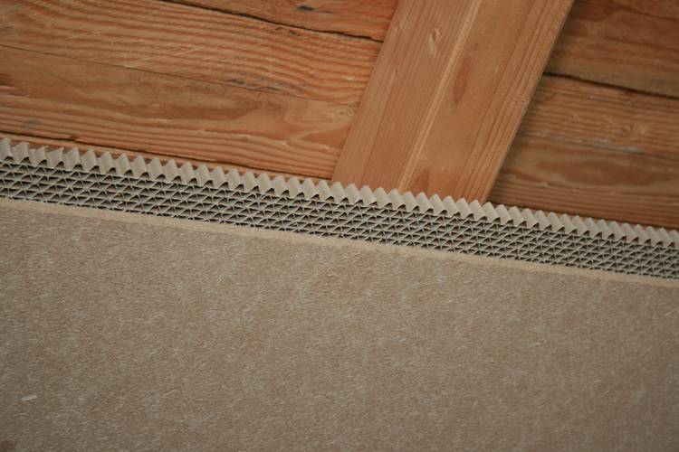 Detailansicht einer Holzbalkendecke mit offener Wärmedämmung und sichtbarer Faserplatte, relevant für energetische Sanierung im Gebäudebestand.