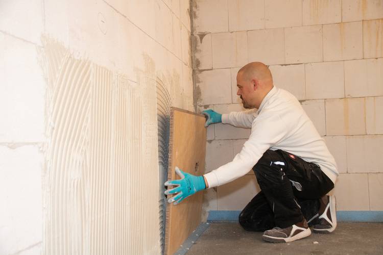 Fachhandwerker montiert eine Wandverkleidung auf Klebefläche im Rohbau, typischer Arbeitsschritt bei Innenausbau und Sanierung in der Gebäudetechnik.