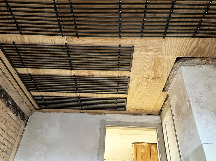 Offene Decke mit sichtbaren Holzpaneelen und parallel verlaufenden schwarzen Leitungen in einem teilsanierten Technikraum, typisch für Gebäudetechnik.