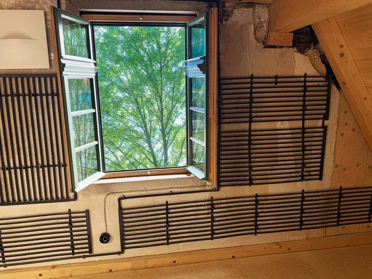 Geöffnetes Fenster in einem rustikalen Raum mit Blick ins Grüne, symbolisiert natürliches Tageslicht und potenzielle Energieeinsparung im Gebäude.