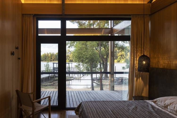 Modernes Schlafzimmer mit großen Fenstern, Blick auf See und Bäume, energieeffiziente Beleuchtung, Holzdekor - Beispiel für nachhaltige Gebäudetechnik.