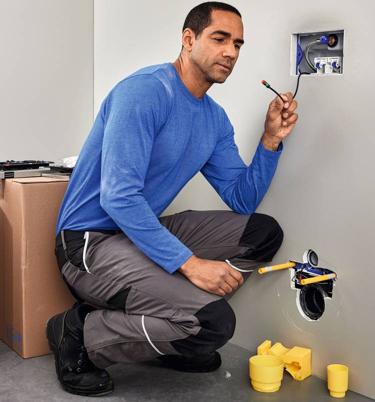 Elektrofachkraft installiert eine Unterputz-Steckdose in einer Trockenbauwand, mit Werkzeug und Installationsmaterialien für Gebäudetechnik.