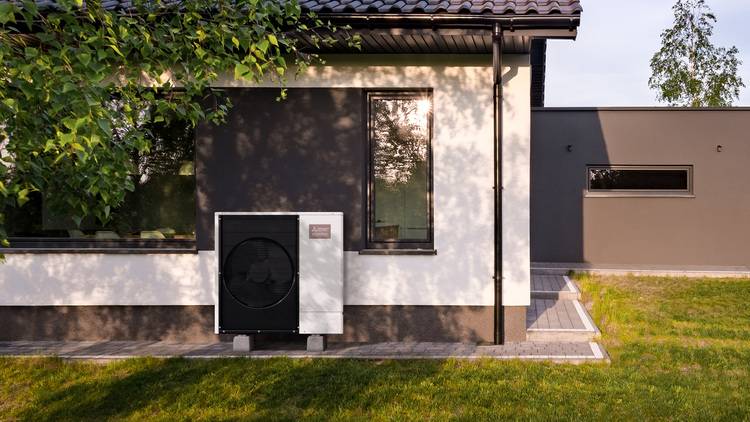 Außen installierte Luft-Wasser-Wärmepumpe vor modernem Gebäude mit weiß-grauer Fassade, beispielhaft für energieeffiziente Gebäudetechnik.