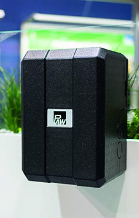 Schwarzes, rechteckiges Wandgerät mit "Paw"-Logo, geeignet für die Gebäudetechnik. Im Hintergrund weiß-grüne Wandgestaltung.