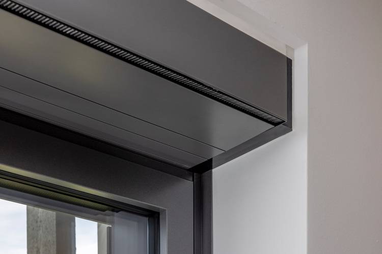 Detailaufnahme eines modernen, dunkelgrauen Metallfensterrahmens in weißer Wand, Fokus auf energieeffiziente Gebäudehülle und Wärmedämmung.