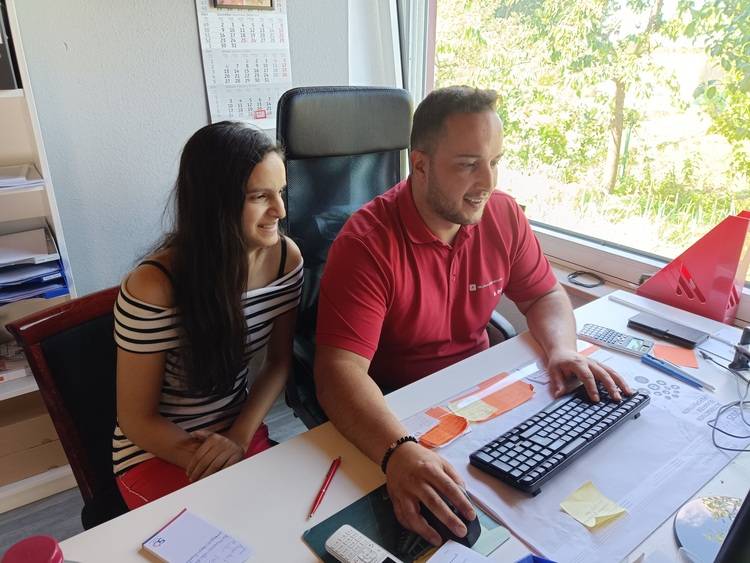 Zwei Fachpersonen aus der Gebäudetechnik-Branche sitzen in einem hellen Büro am Schreibtisch und besprechen Baupläne am Computer.