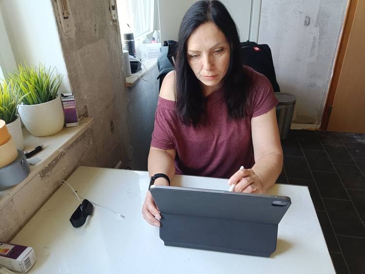 Fachplanerin für Gebäudetechnik mit Tablet und Stylus am Schreibtisch, prüft digitale Baupläne in hellem Büro mit unfertigen Wänden.