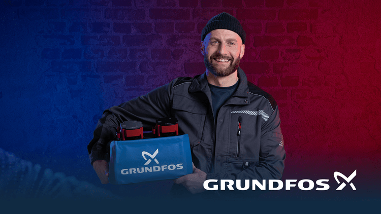Fachhandwerker in Arbeitskleidung präsentiert blaue Grundfos-Tasche vor gemauerter Wand, Symbol für Gebäudetechnik-Lösungen und SHK-Partner.
