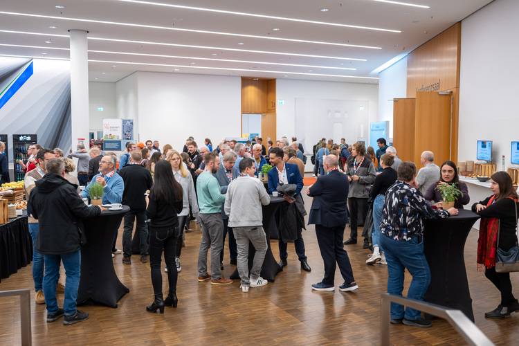 Fachpublikum aus der Gebäudetechnik beim Netzwerken auf einer Branchenmesse, Gesprächsrunden an Stehtischen, Fokus auf beruflichen Austausch.