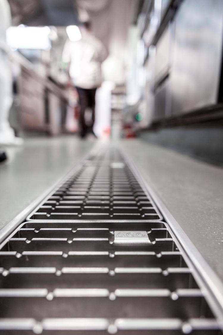 Bodenablauf aus Edelstahl in einer gewerblichen Küche, Fokus auf Entwässerungstechnik für Hygienestandards im SHK-Bereich, Hintergrund unscharf.