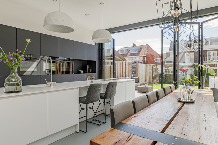 Moderne Wohnküche mit schwarzen Schränken, weißer Kochinsel und Holz-Esstisch, große Fenster sorgen für Tageslicht - Beispiel energieeffizienter Innenausbau.