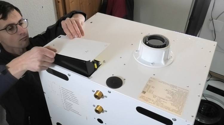 Fachkraft montiert eine Serviceklappe an einer großen weißen Kälte- oder Lüftungsanlage in einer Werkstatt für Gebäudetechnik.