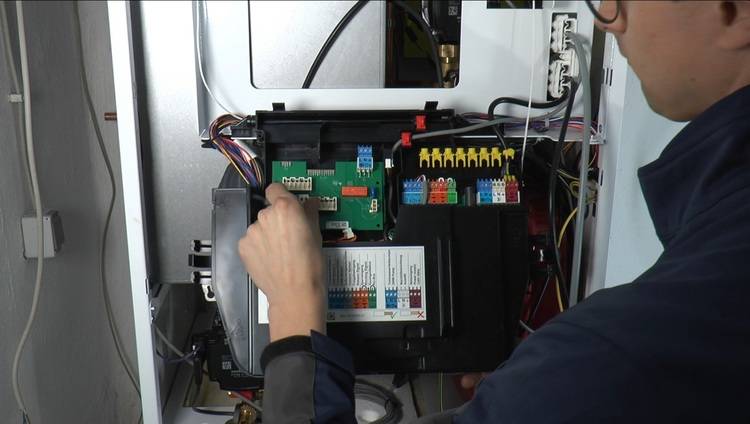 Fachkraft prüft offenliegende Verkabelung und Leiterplatten in einem geöffneten Schaltschrank, Fokus auf Gebäudetechnik-Installation und Sicherheit.