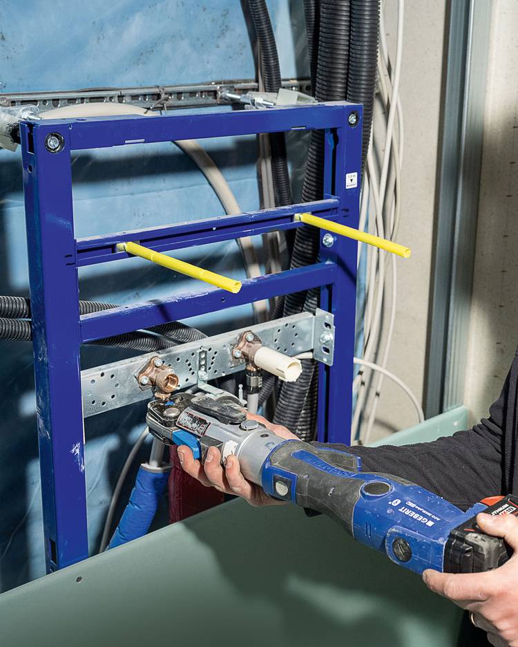 Montage einer Rohrinstallation: Fachkraft schneidet mit blauem Elektrowerkzeug Metallrohre im wandmontierten Installationsrahmen zu.