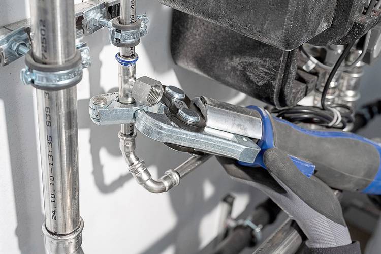 Fachgerechtes Anziehen eines Rohrfittings an einer Metallinstallation durch einen Monteur mit Arbeitshandschuh und passendem Werkzeug im SHK-Bereich.
