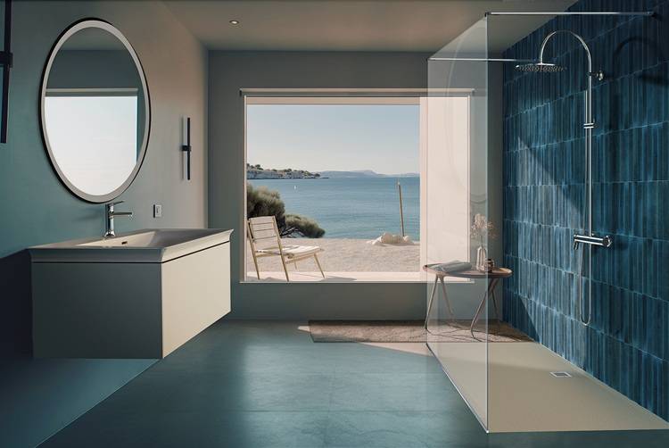 Modernes Badezimmer mit großem Fenster, Blick aufs Meer, barrierefreier Duschzone mit blauen Fliesen. Außenbereich: Freisitz auf Sandboden.