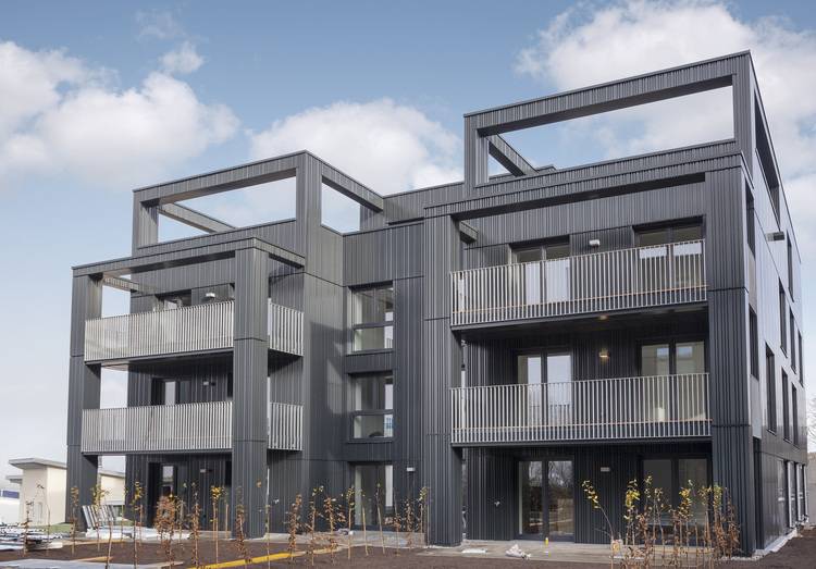 Mehrgeschossiges, modernes Wohngebäude mit dunkler Fassade und großen Balkonen, Beispiel für energieeffiziente Gebäudehülle in urbaner Umgebung.