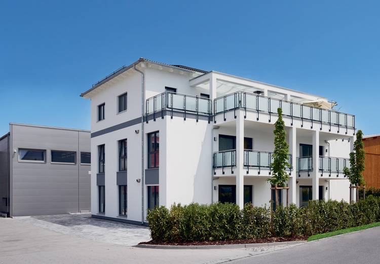 Modernes, energieeffizientes Wohngebäude mit großen Fenstern und Balkonen, umgeben von Begrünung - Beispiel für nachhaltige Gebäudetechnik.