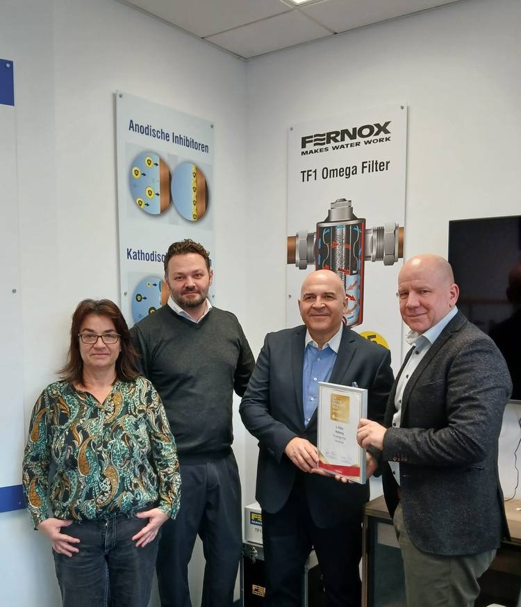 Vier Fachleute aus der Gebäudetechnik bei einer Auszeichnung; ein Mann hält eine Urkunde, technische SHK-Poster hängen im Hintergrund.