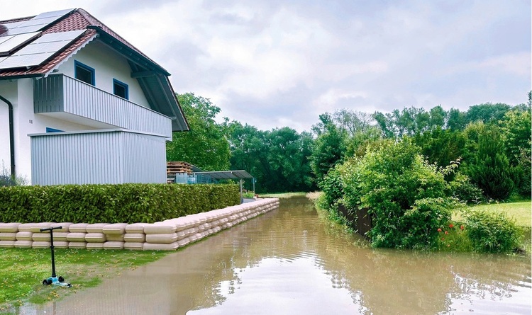 Hochwasser auf einer Straße neben einem mit Sandsäcken gesicherten Gebäude - Schutzmaßnahmen gegen Überflutung im Bereich Gebäudetechnik.