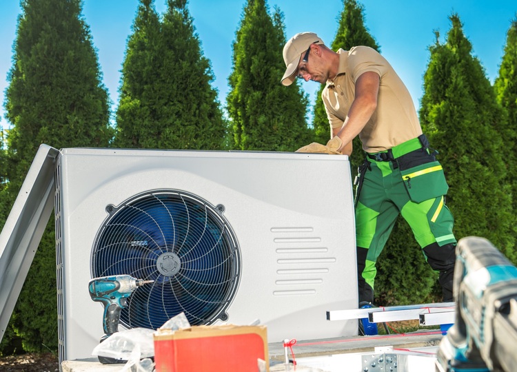 Fachkraft wartet eine Außeneinheit einer Klimaanlage im Freien, relevanter Kontext für Gebäudetechnik, Energieeffizienz und Wartungsmanagement.