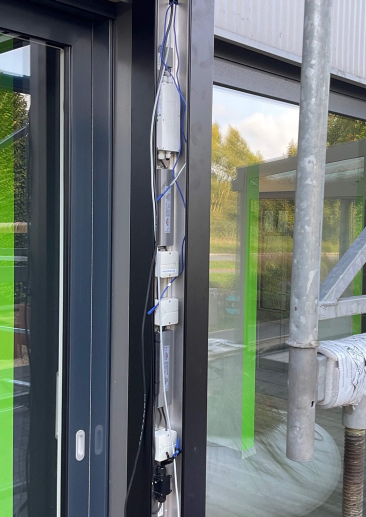 Vertikal montierte Kabel und Steuerungseinheiten zur Gebäudeautomation an schwarzem Türrahmen, neben einer Schiebetür im modernen Technikraum.