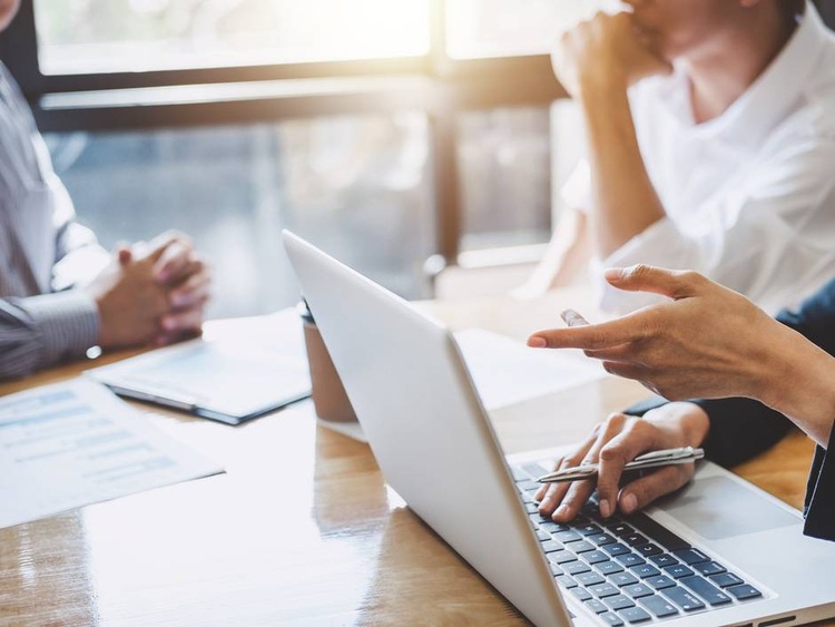 Drei Fachleute der Gebäudetechnik bei einer Besprechung am Tisch mit Laptop, Unterlagen und Kaffee in modernem, lichtdurchflutetem Büro.