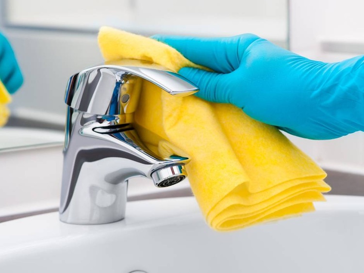 Fachkraft mit Schutzhandschuh reinigt Armatur im Sanitärbereich mit gelbem Tuch - Hygienemaßnahme für Gebäudetechnik und Facility Management.