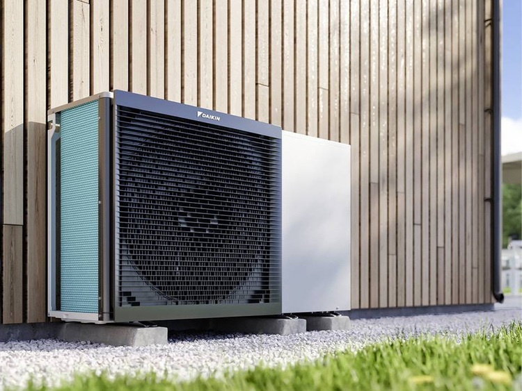 Luft-Wasser-Wärmepumpe, außen auf Kiesfläche vor Holzfassade installiert, zeigt energieeffiziente Heiztechnik für Gebäudetechnik-Fachpublikum.