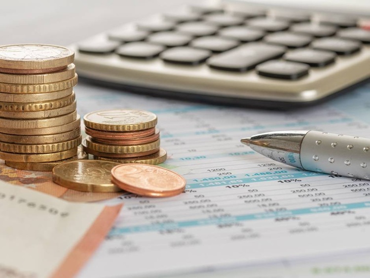 Symbolbild für Investition, Kostenkalkulation und Wirtschaftlichkeit in der Gebäudetechnik: Münzstapel, Kugelschreiber und Taschenrechner auf Finanzunterlagen.