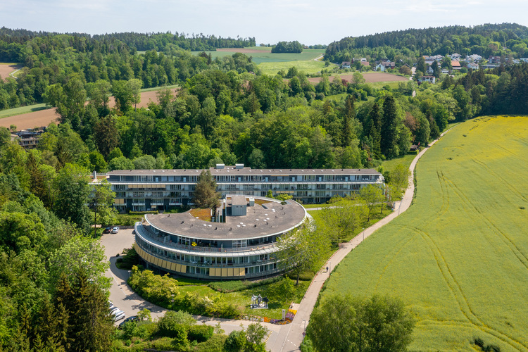 Luftaufnahme eines modernen, geschwungenen Gebäudes in ländlicher Umgebung, beispielhaft für energieeffiziente Architektur in der Gebäudetechnik.