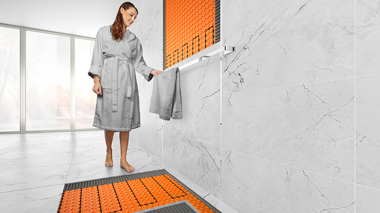 Moderne Badinstallation mit elektrisch beheizten, orangefarbenen Bodenfliesen und großformatigen Marmorwänden als Beispiel energieeffizienter Gebäudetechnik.