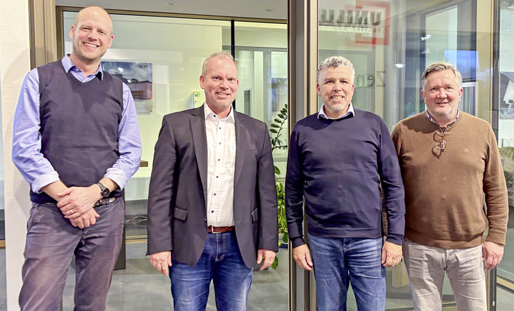 Vier Fachleute der Gebäudetechnik in Business Casual, stehend vor großen Fenstern, auf Branchenevent oder Fachtagung zu SHK und Energieeffizienz.