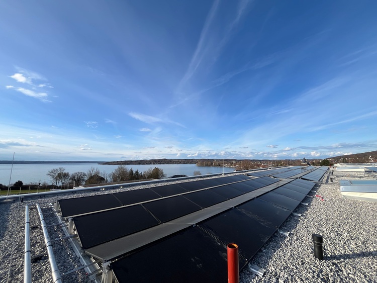Photovoltaikanlage auf einem modernen Flachdach, im Hintergrund See und Ufer; Fokus auf erneuerbare Energien und Gebäudeeffizienz in der TGA.