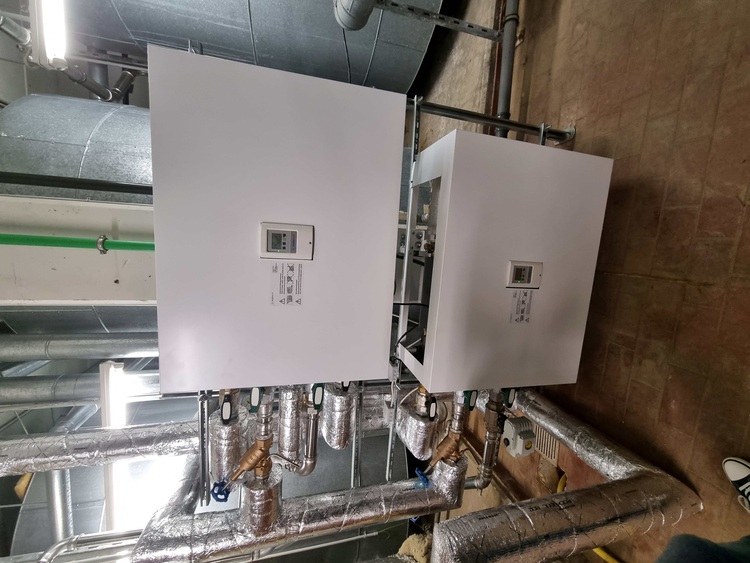 Zwei weiße Steuerungs- und Bedientafeln mit Digitalanzeigen sind in eine Rohrinstallation einer gebäudetechnischen Anlage integriert.